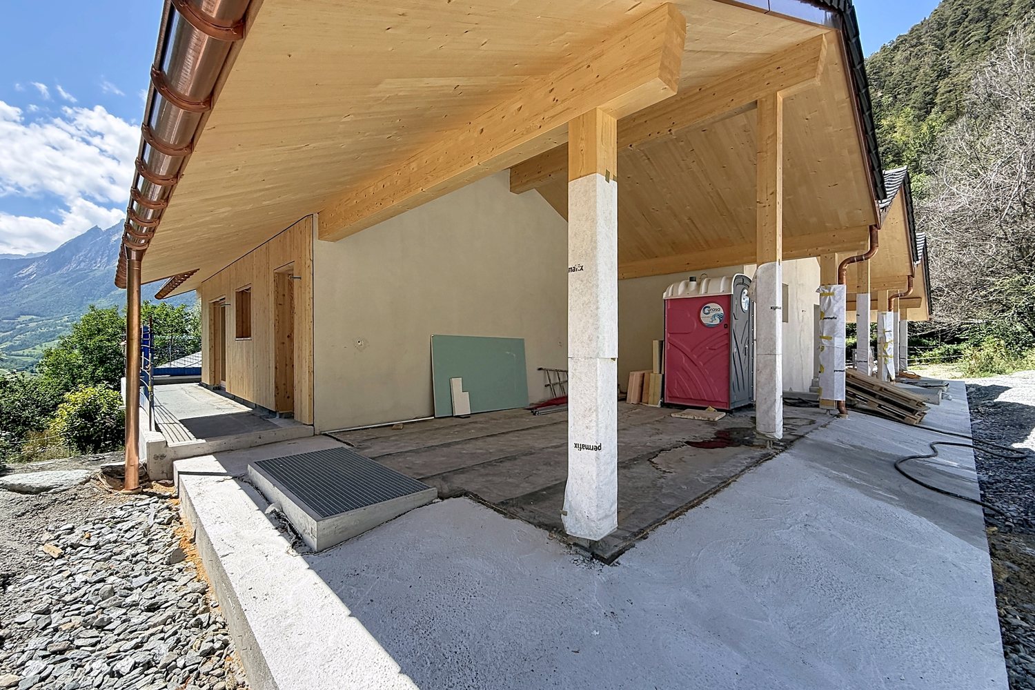 Couvert extérieur soutenu par des piliers, charpente en bois clair.